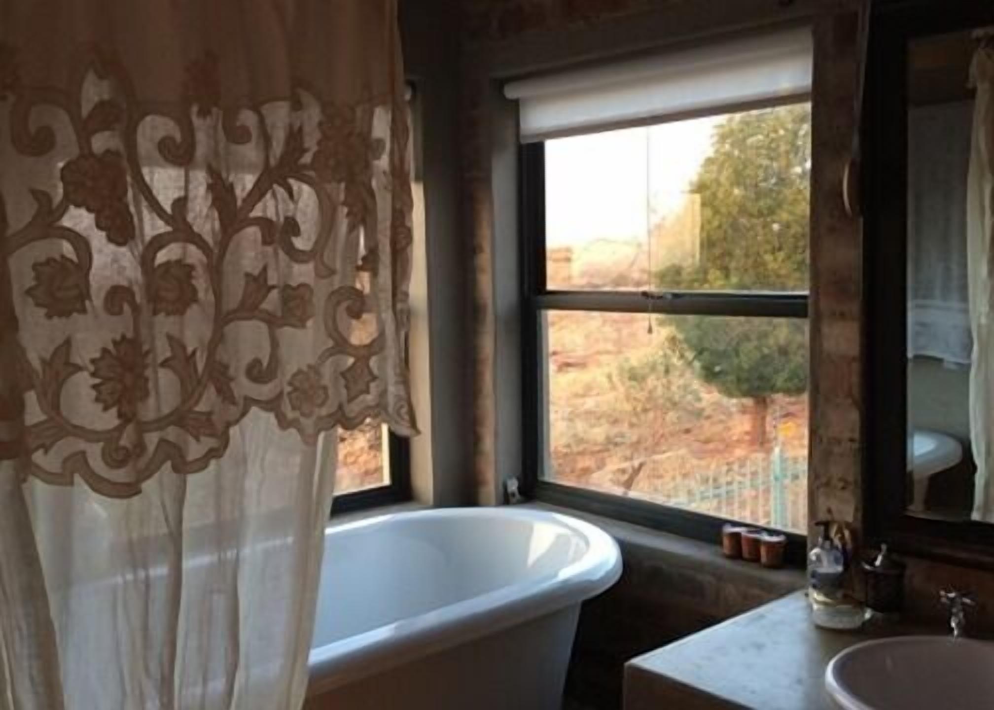 Une salle de bain avec une grande baignoire, une fenêtre donnant sur un paysage aride et un lavabo avec un miroir.
