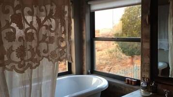Une salle de bain avec une grande baignoire, une fenêtre donnant sur un paysage aride et un lavabo avec un miroir.