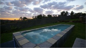 A rectangular swimming pool with a stone border, surrounded by a grassy lawn and a stone wall. - The Warehouse (Krugersdorp)