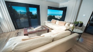 Ein modernes Wohnzimmer mit einem beigen Sofa, einem Couchtisch und Blick durch große Glasfenster.