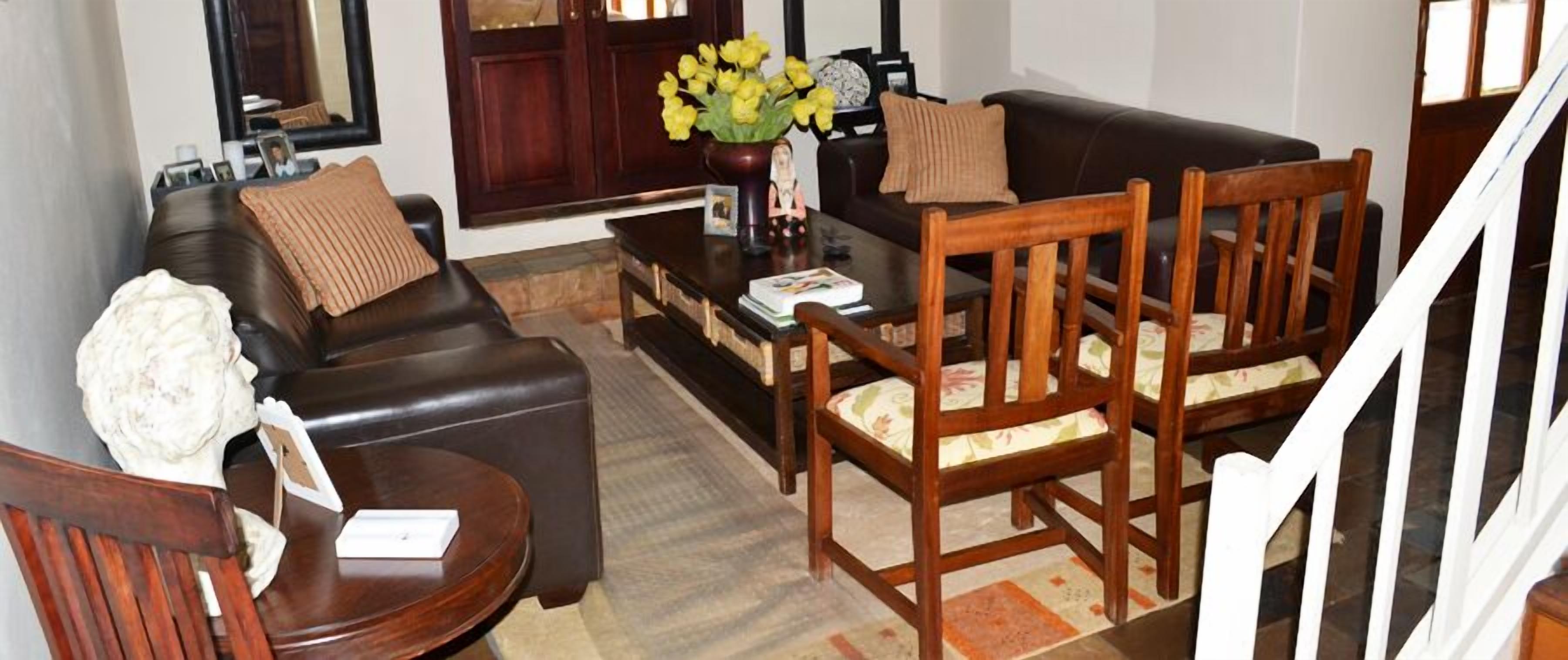 A living room with a black leather sofa, wooden chairs, a coffee table, and a vase with yellow flowers.