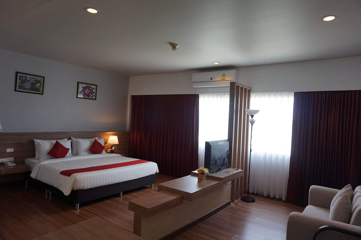 A hotel room with a bed, a desk, a chair, a TV, and an air conditioning unit.