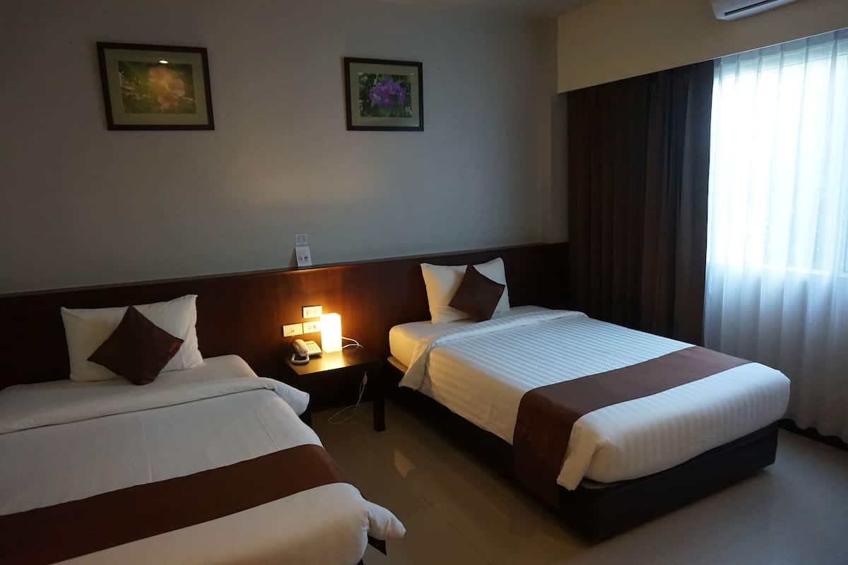 A hotel room with two beds, a nightstand with a lamp, and two framed pictures on the wall.