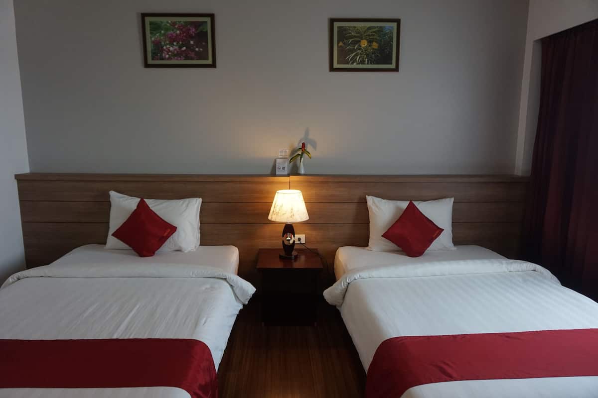A hotel room with two beds, a nightstand with a lamp, and two framed pictures on the wall.
