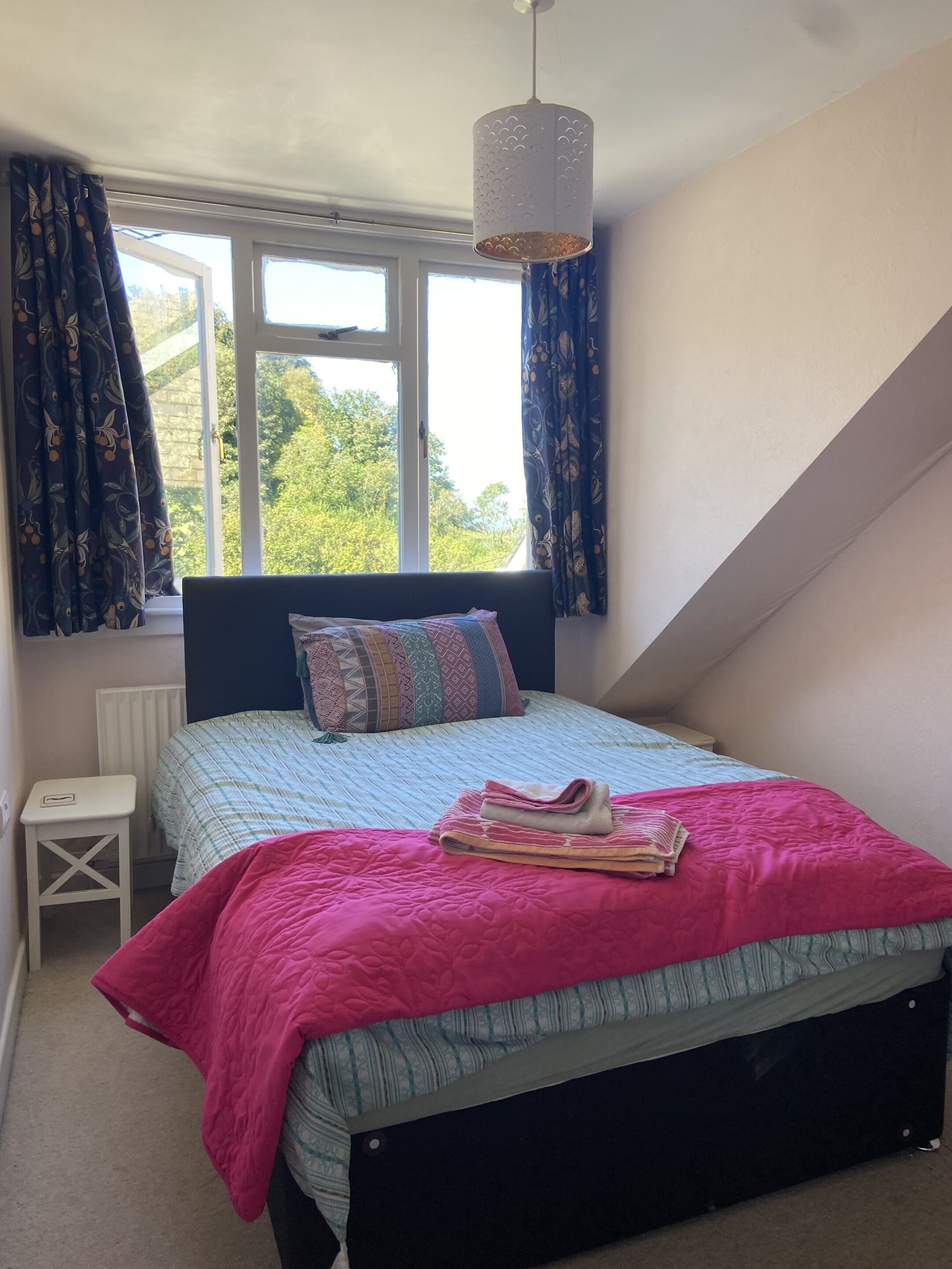 A bedroom with a bed, a bedside table, a radiator, and a window with curtains.