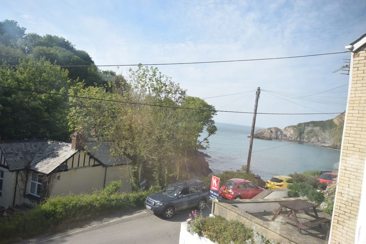 Une route côtière bordée de voitures garées, une pancarte « À vendre » et une vue sur la mer.
