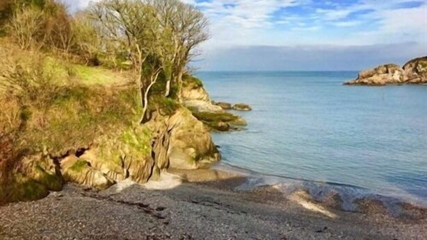 A coastal landscape with rocky cliffs, a pebbly beach, and a clear blue sea under a partly cloudy sky. - Newberry Beach Lodge (Ilfracombe)