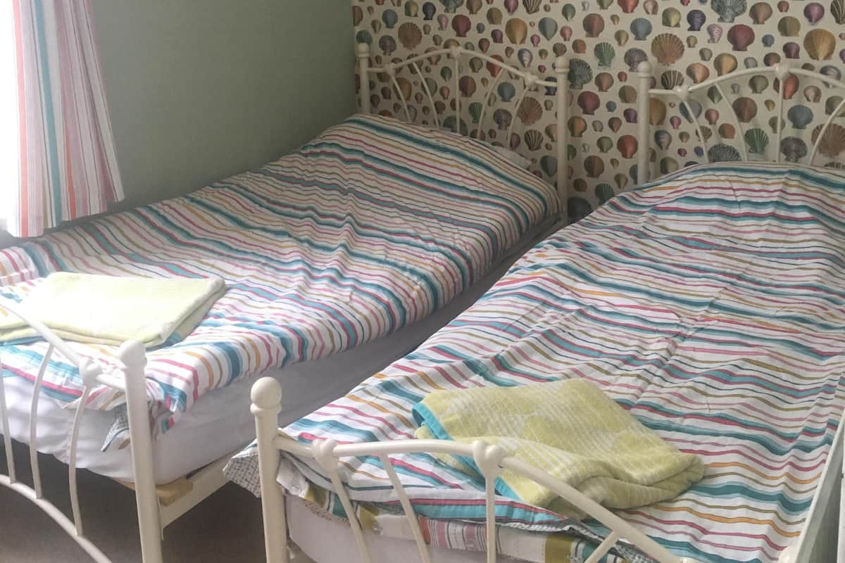 Une chambre avec deux lits simples, un papier peint à motifs et un rideau.