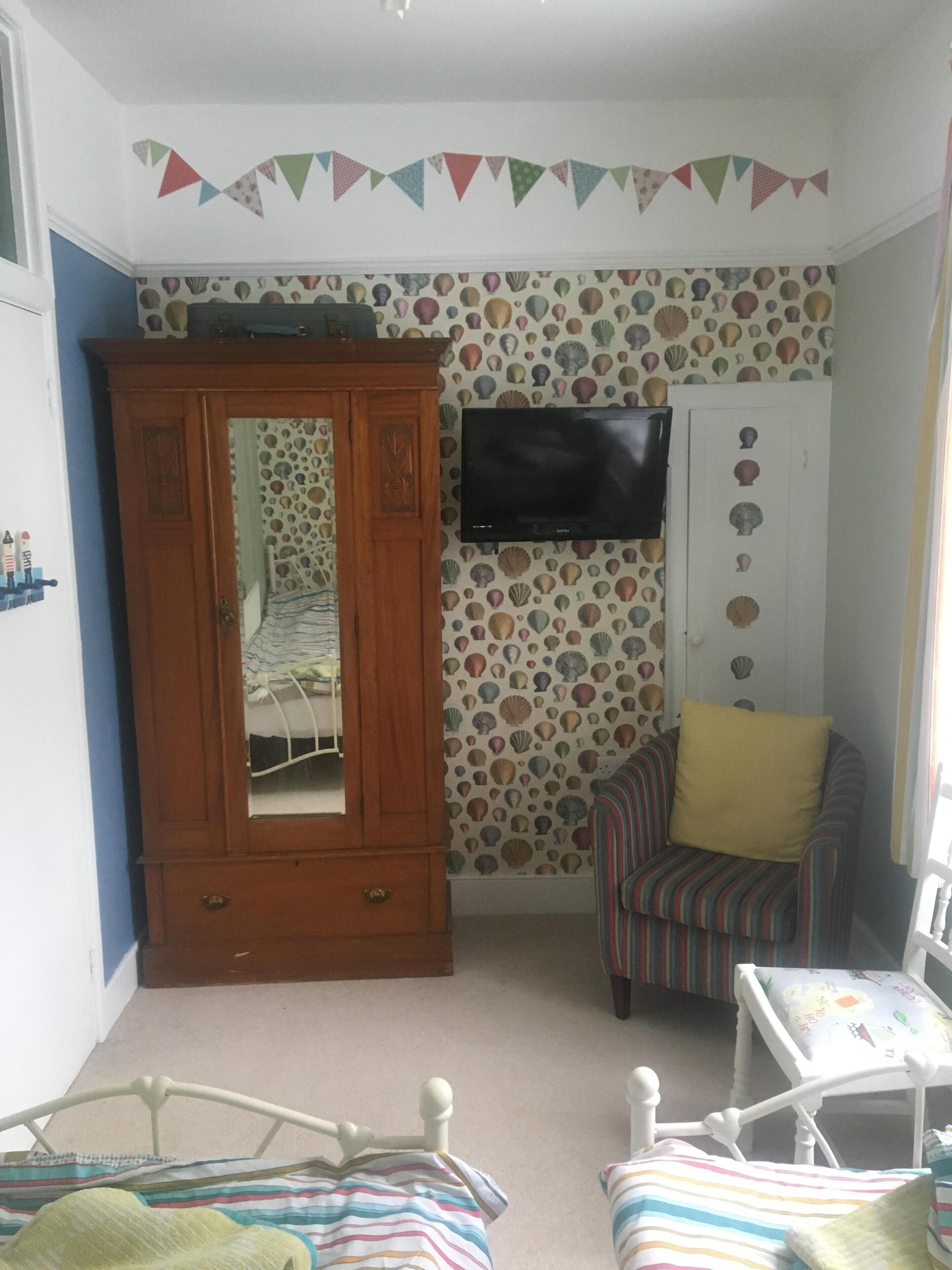 A child's bedroom with a wooden wardrobe, a television, a striped chair, and a bed.