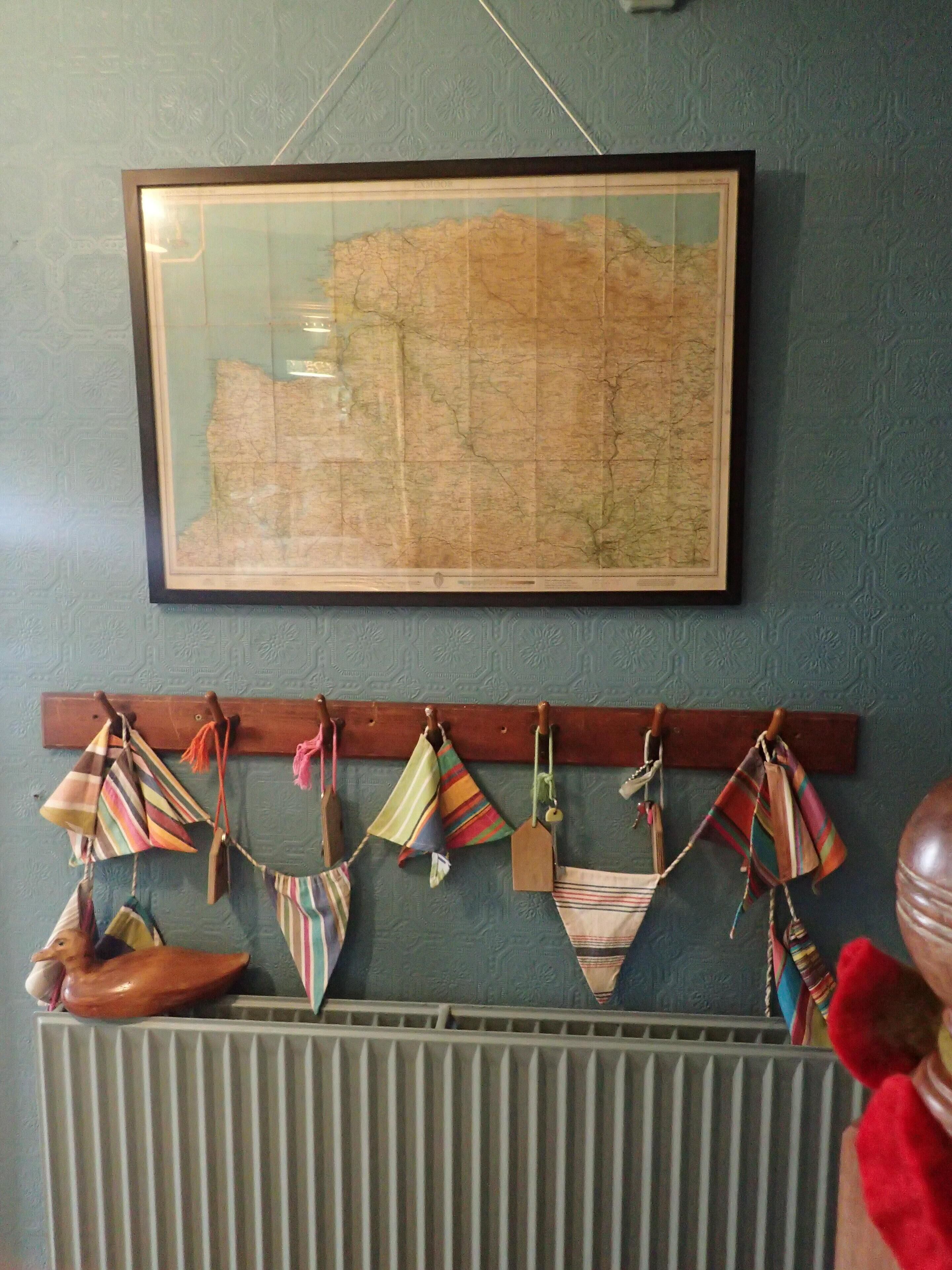 Un mapa enmarcado en la pared, un radiador debajo y un perchero con varias bolsas y una bota.
