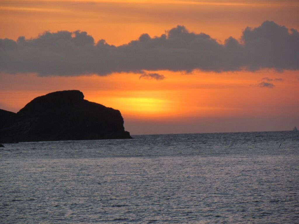 A sunset over a body of water with a prominent rock formation on the left.