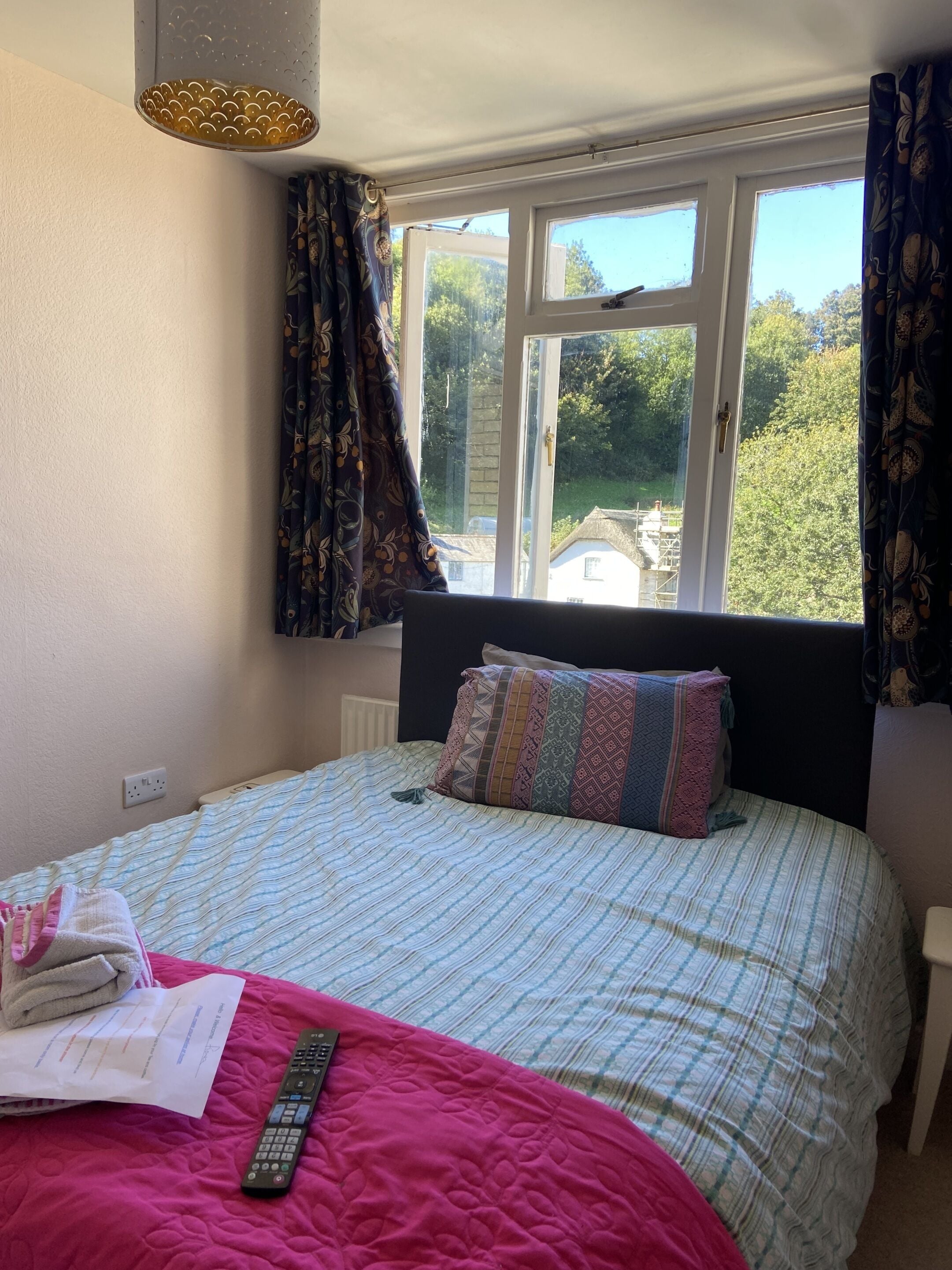 A bedroom with a bed, a window with curtains, a bedside table, and a lamp.
