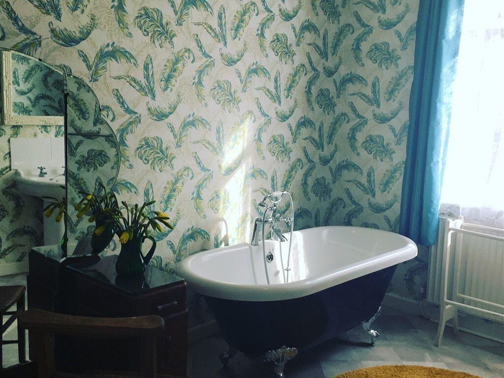 A bathroom with a freestanding bathtub, a mirror, a sink, and a vase with flowers.