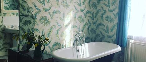 A bathroom with a freestanding bathtub, a mirror, a sink, and a vase with flowers.
