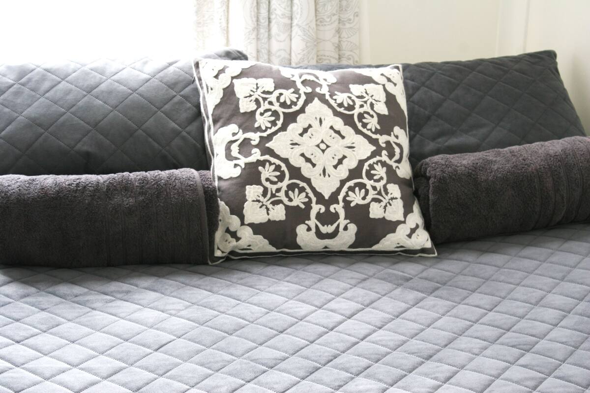 Un lit avec un matelas matelassé de couleur grise et deux oreillers, dont l’un est à motifs floraux et l’autre est uni.