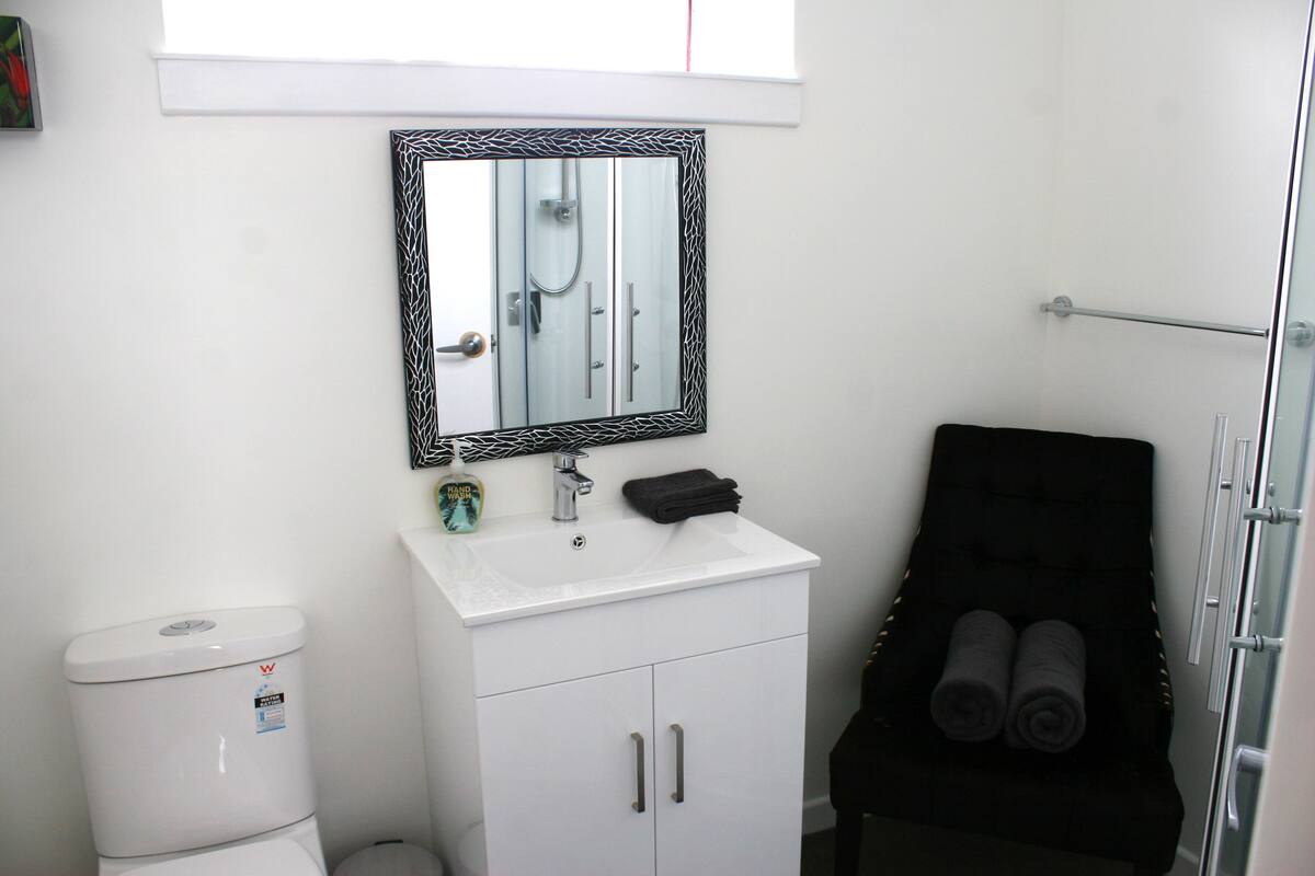 Une salle de bain avec un lavabo blanc, un miroir avec un cadre noir, un porte-serviettes noir et un banc noir pour les serviettes.