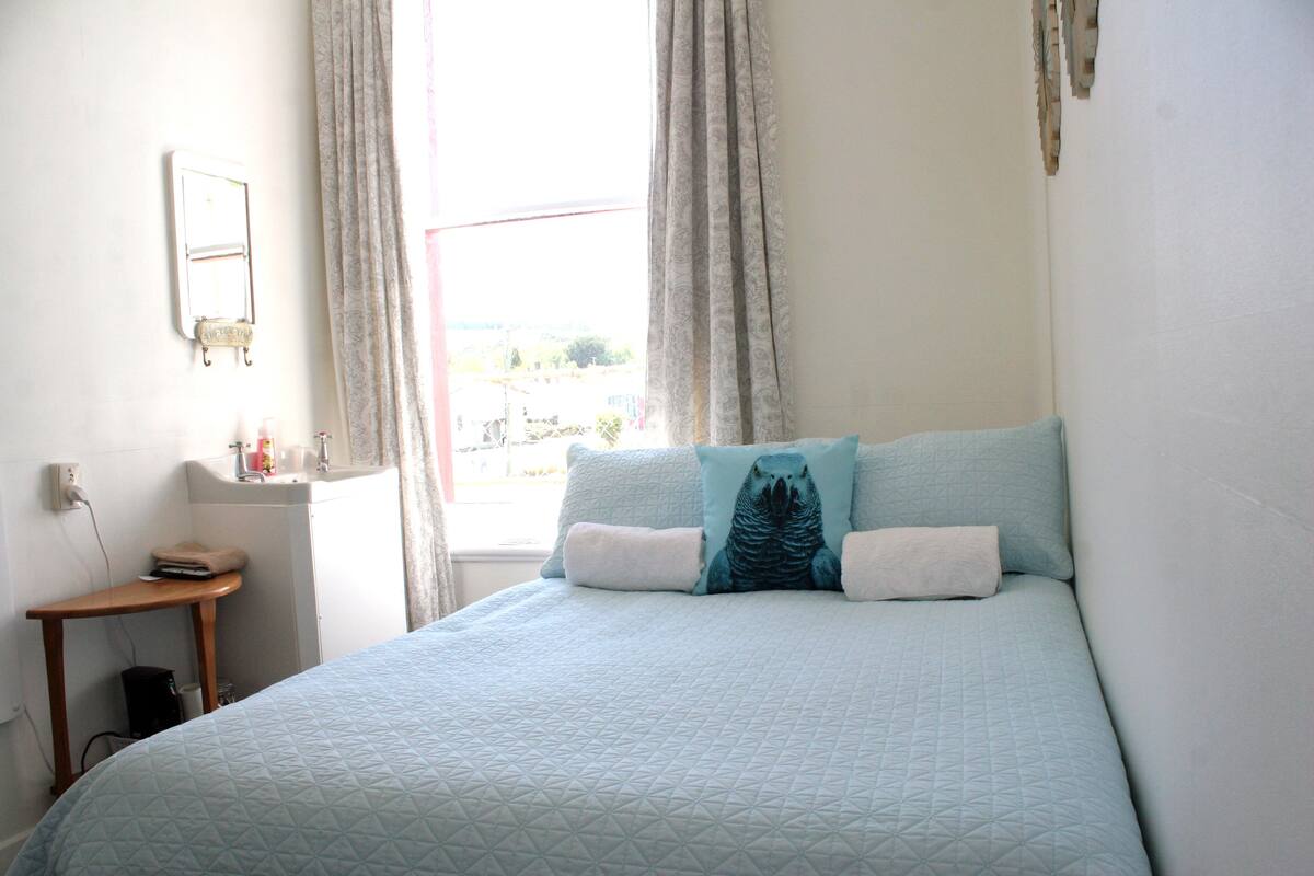Une chambre à coucher avec un lit, une table de chevet, un miroir et une fenêtre avec des rideaux.