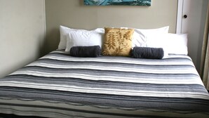 A bed with striped bedding, two pillows, and a wall-mounted painting. - Lumsden Hotel (Lumsden)