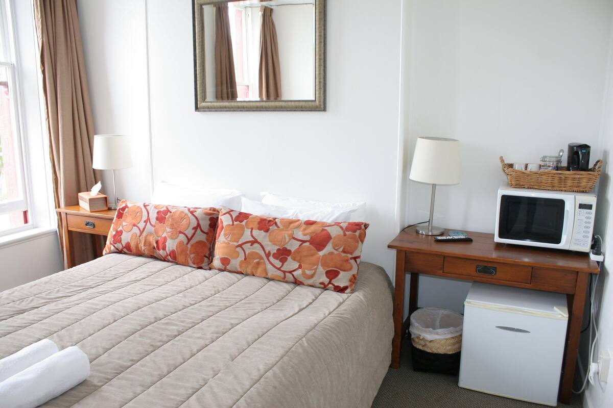 Une chambre d’hôtel équipée d’un lit, d’un bureau avec un micro-ondes, d’une poubelle et d’un petit réfrigérateur.