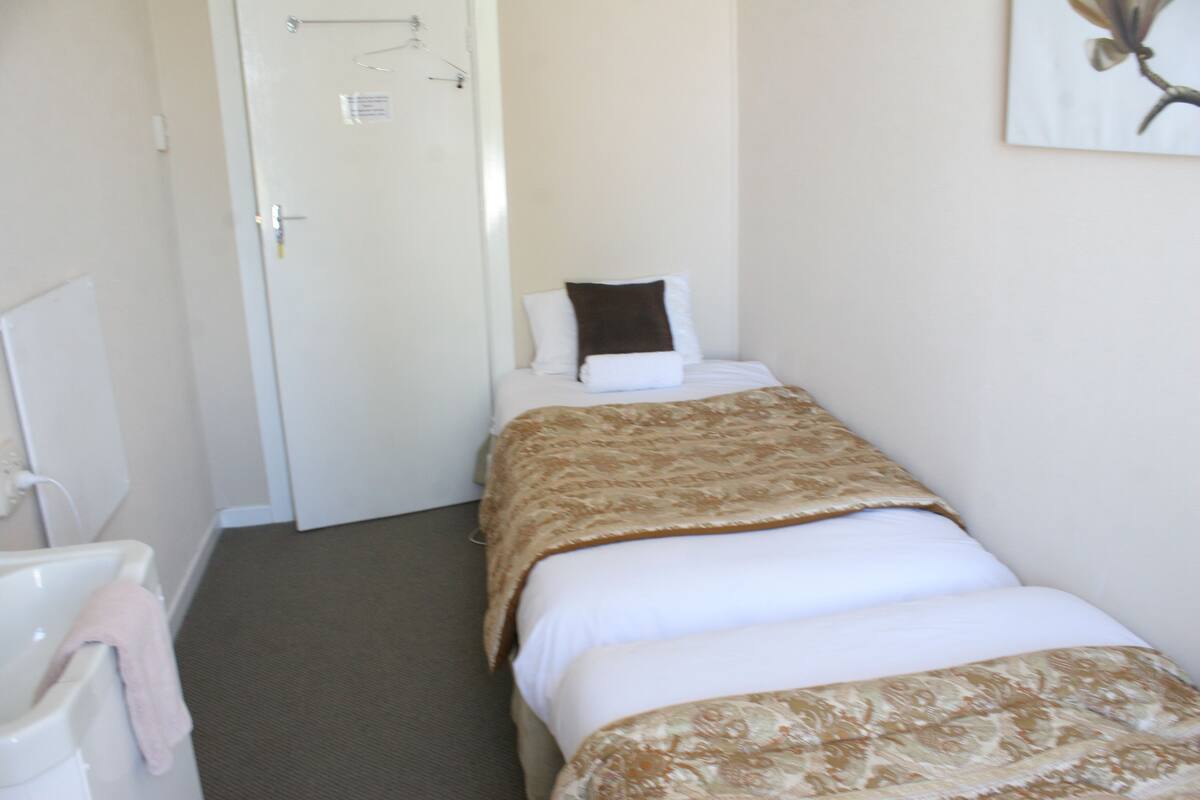 Une petite chambre à coucher, bien rangée, avec un lit simple, une table de chevet et une porte donnant sur une autre pièce.