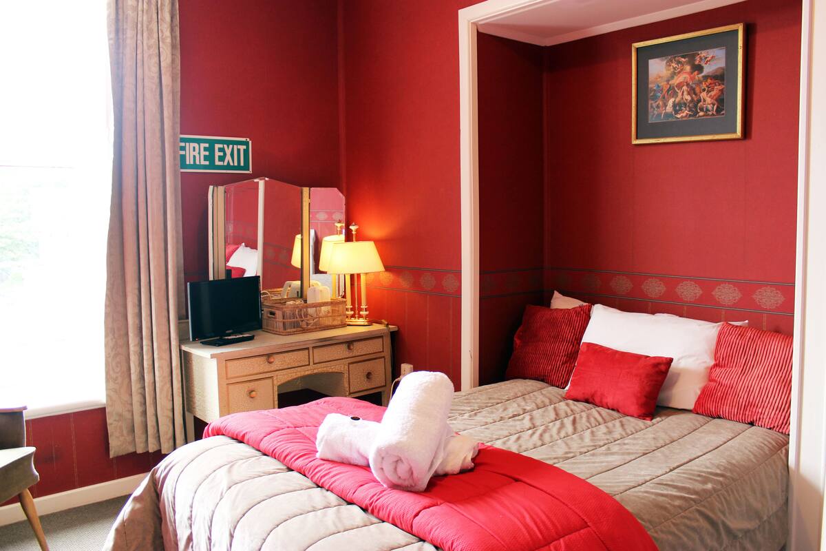 Une chambre d’hôtel avec un lit, un bureau doté d’une lampe, une télévision et un panneau indiquant la sortie de secours.