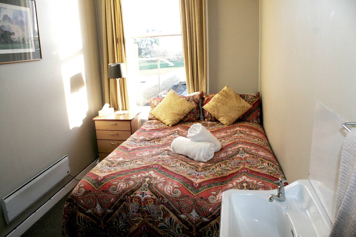 Une chambre d’hôtel comprenant un lit, une table de chevet avec une lampe, une fenêtre avec des rideaux et une salle de bain avec une baignoire.