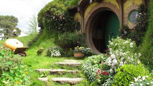 A Hobbit-style house with a round door, stone steps leading up to it, and a garden with various plants and flowers. - Rolling Hills Country Stay B&B (Oropi)