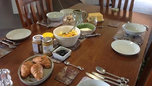 A dining table set with plates, bowls, and utensils, with a bowl of fruit and croissants on the table. - Rolling Hills Country Stay B&B (Oropi)