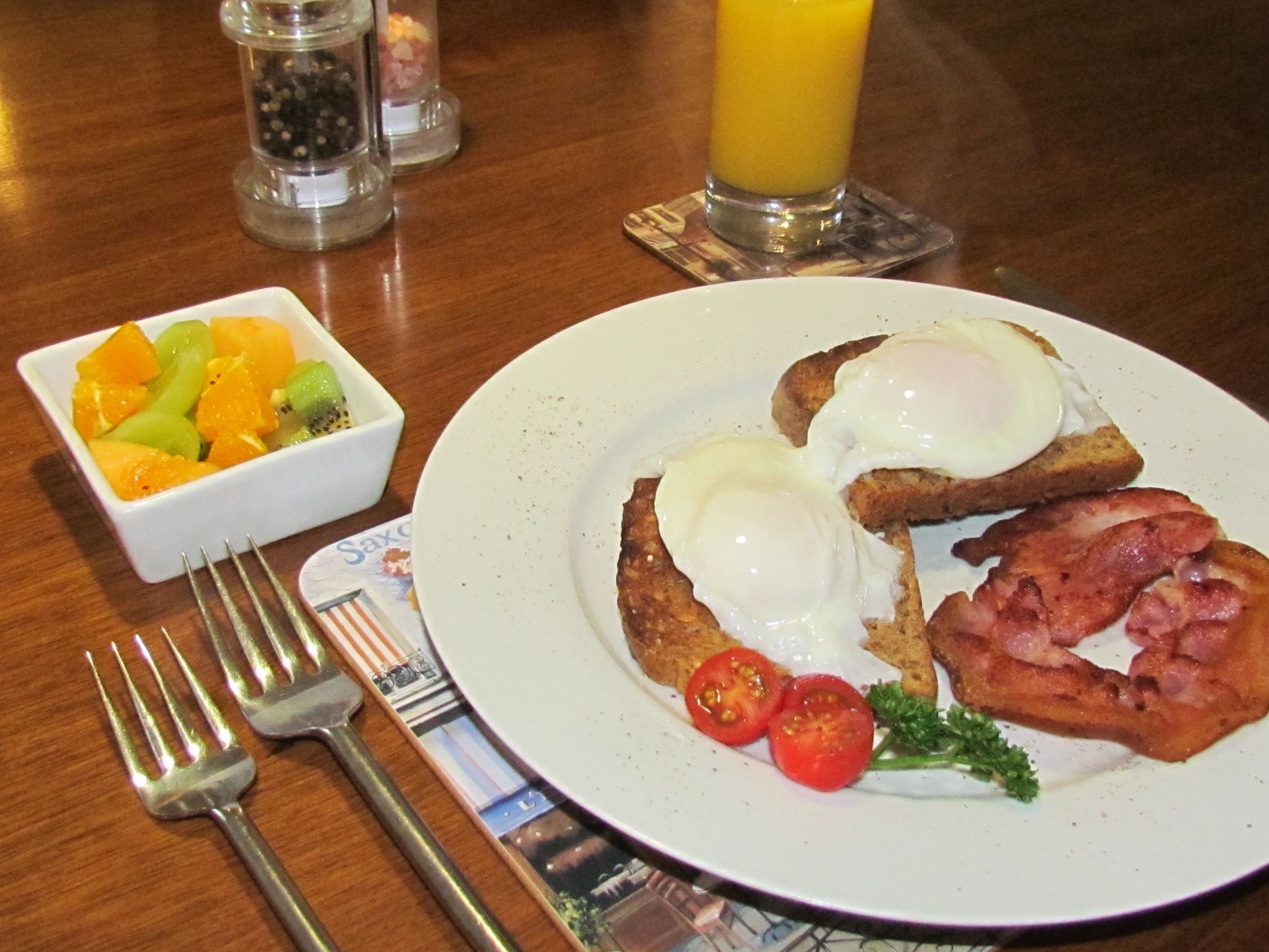 A breakfast plate with eggs, bacon, tomatoes, and a side of fruit salad.