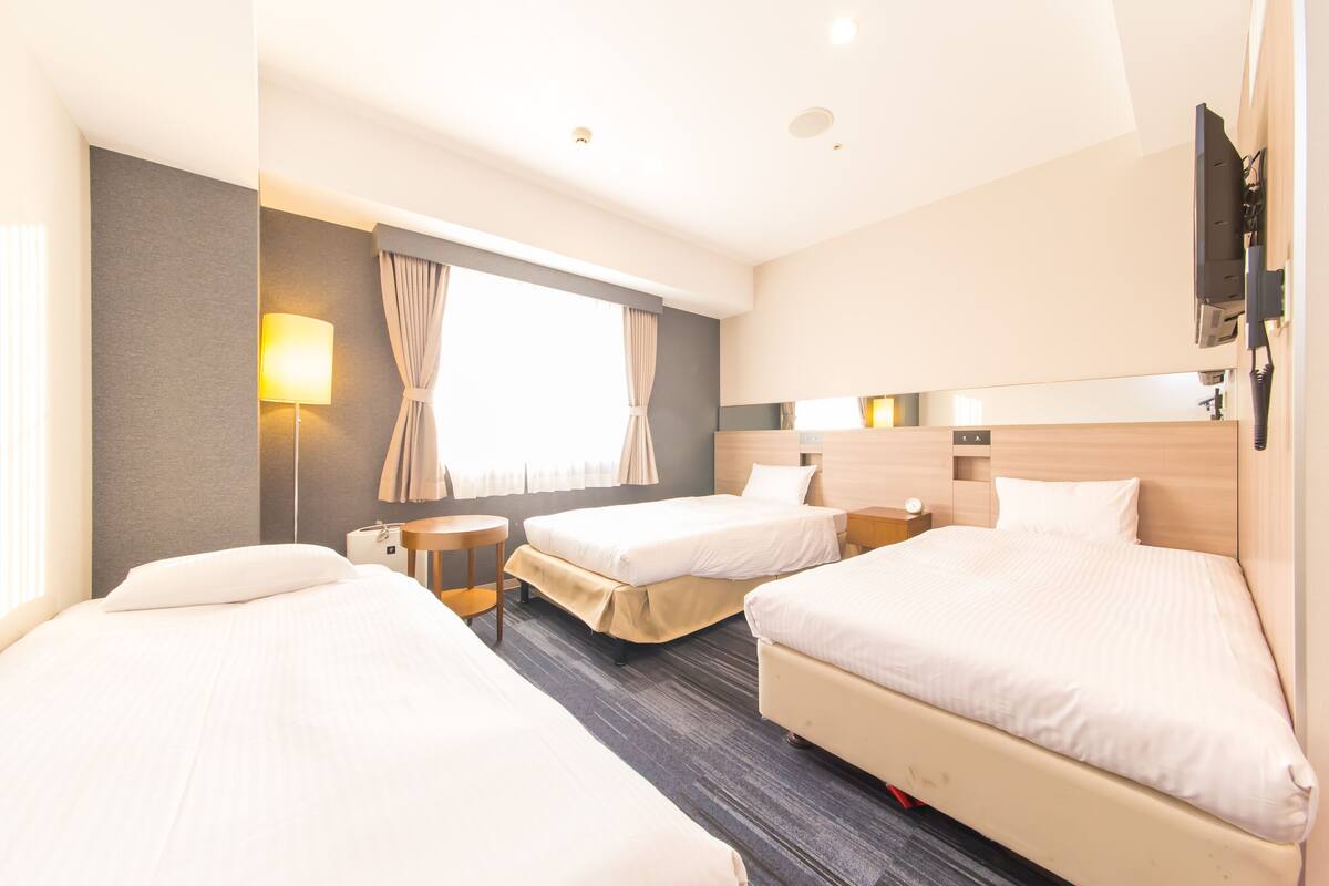 A hotel room with two beds, a desk, a lamp, and a TV mounted on the wall.