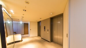 A hallway with a mirrored wall, a white bench, and two elevators. - Hotel IL Cuore Namba (Osaka)