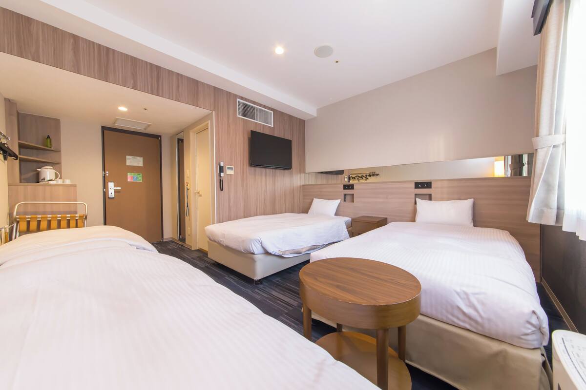 A hotel room with two beds, a TV, a small table, and a shower area.
