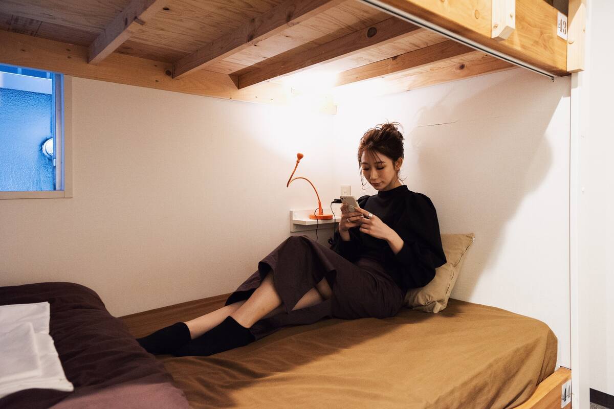 Una persona sentada en una cama en una habitación con techo inclinado y una ventana.