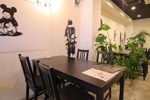 A dining area with a black table and chairs, a menu on the table, and wall art including a cartoon character and a silhouette.