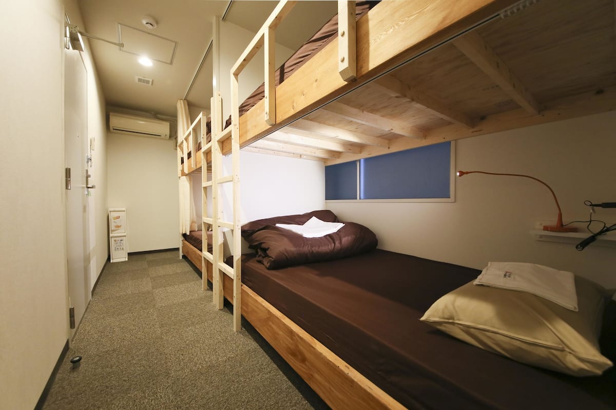 Habitación tipo dormitorio con literas, una ventana pequeña y un escritorio con lámpara.