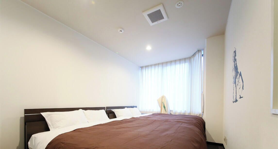 Ein Hotelzimmer mit einem großen Bett, einem Fenster mit Vorhängen, einem an der Wand befestigten Kunstwerk und einem Deckenlüfter.