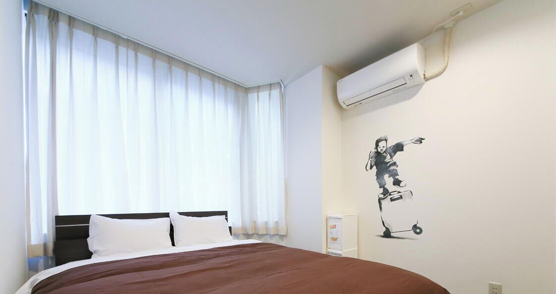 Ein Hotelzimmer mit Bett, weißen Vorhängen, einer Klimaanlage und einem Wandbild.