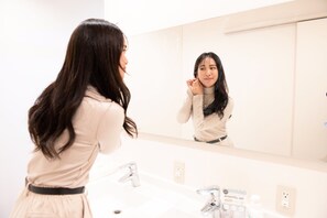 A woman in a beige dress standing in front of a bathroom sink and mirror.