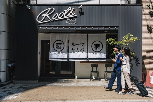 The exterior of a hostel named 'Roots Hostel' with a sign indicating it offers lodging and a bar.