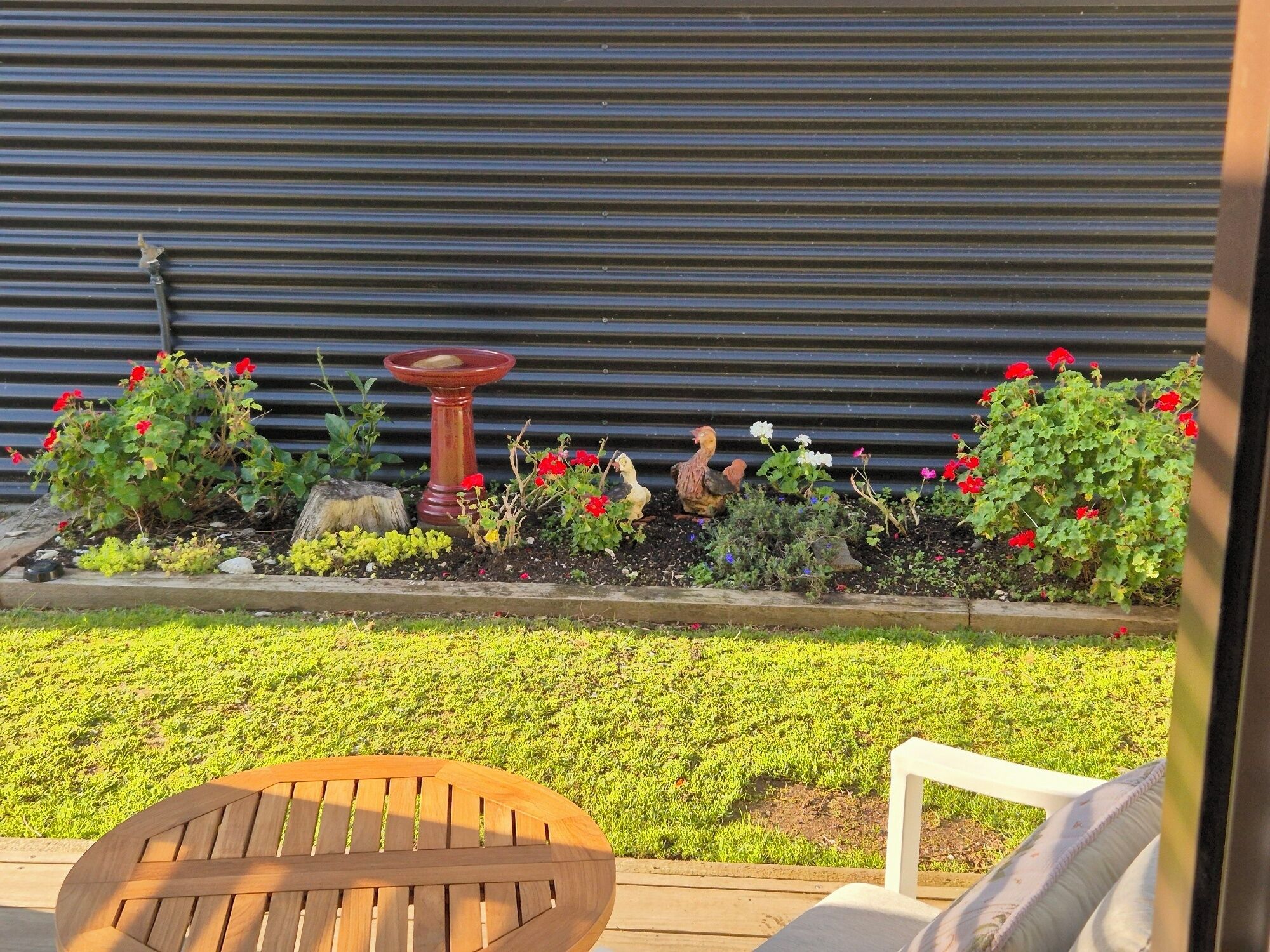 A garden with a wooden bench, a bird bath, and various plants and flowers.
