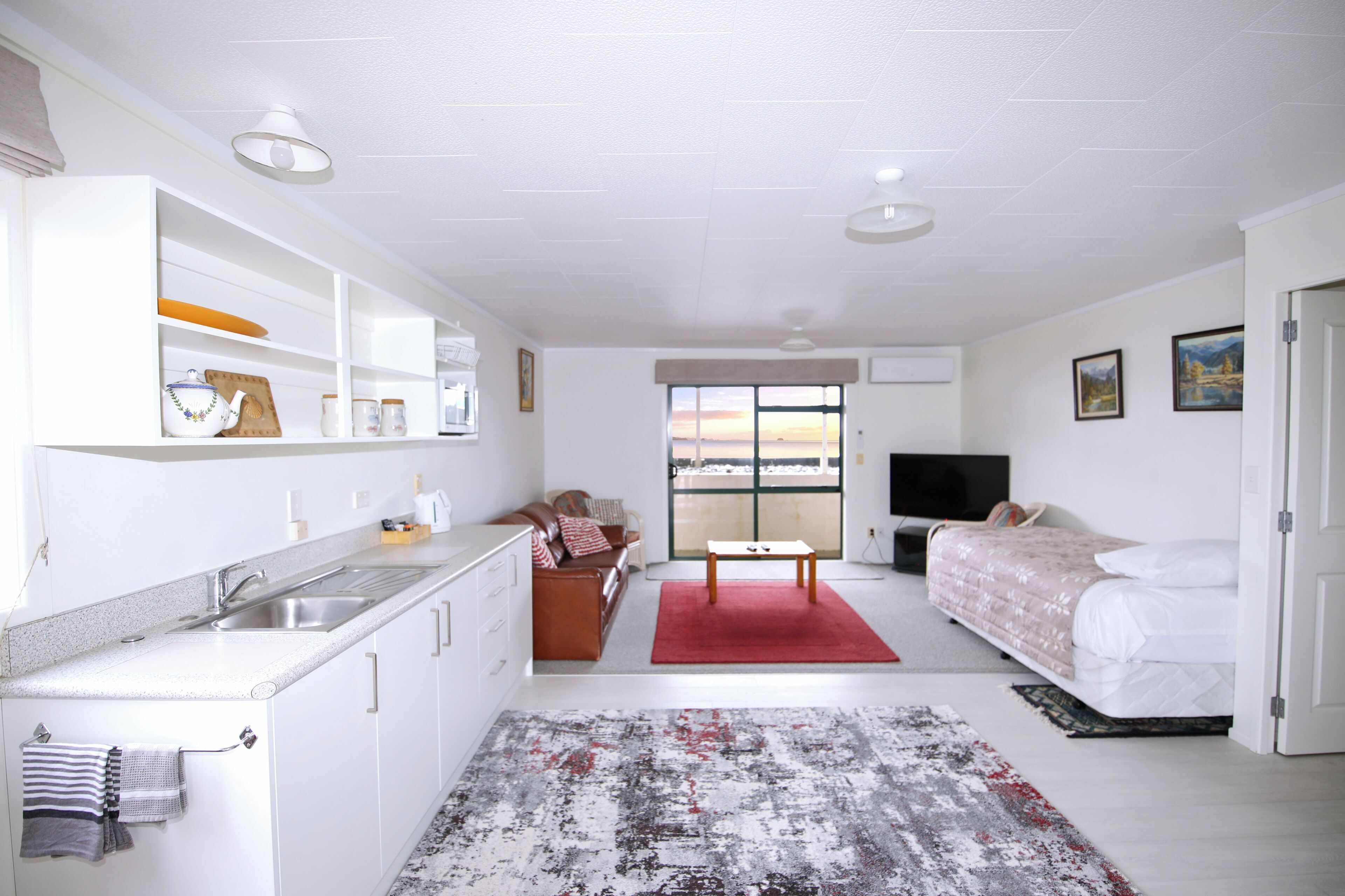 A modern, well-lit room with a kitchenette, a dining area, and a bed.