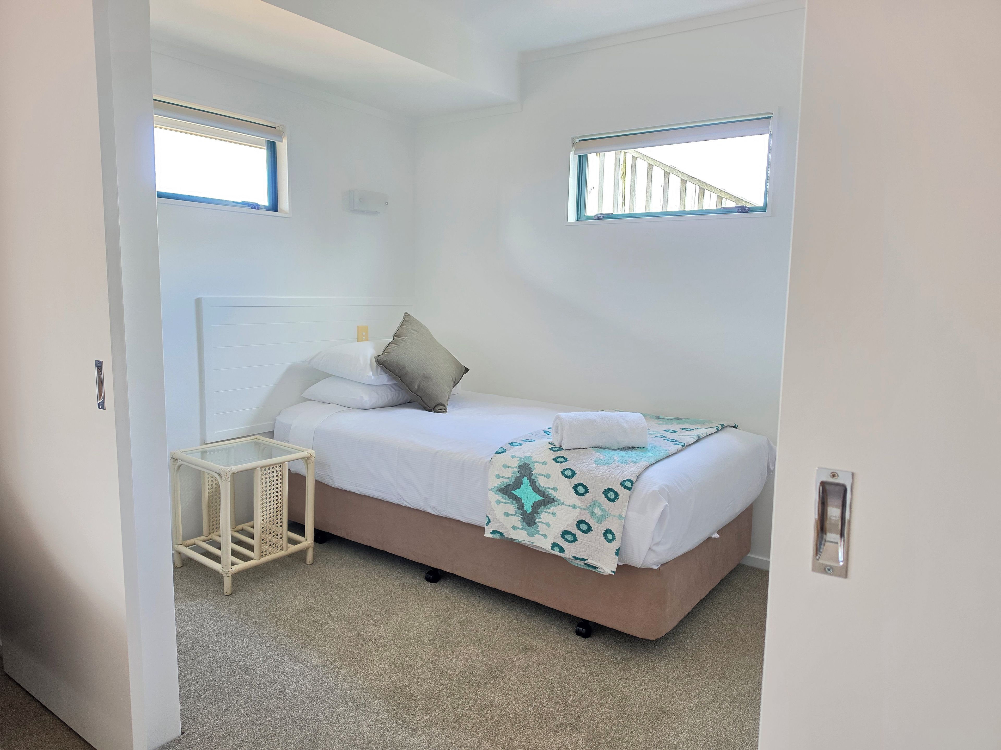 A bedroom with a bed, a bedside table, a window, and a door.