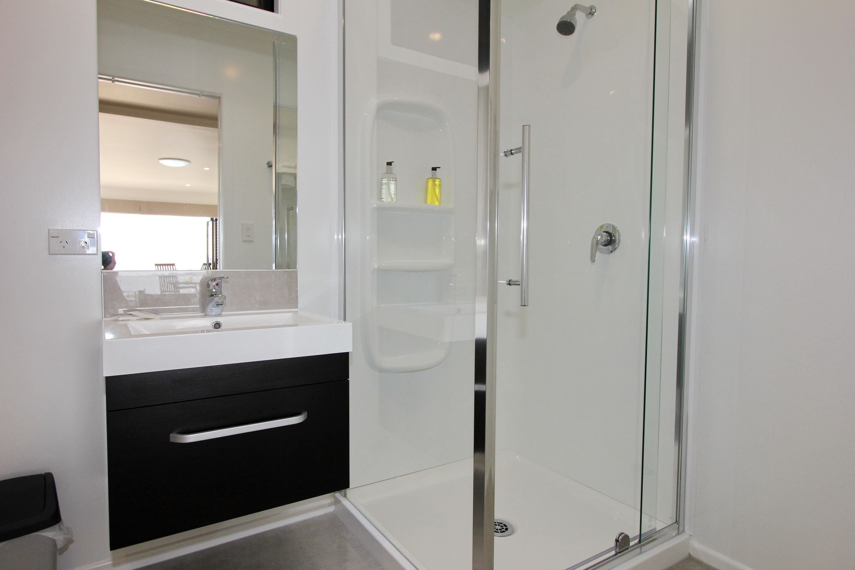 A modern bathroom with a glass shower enclosure, a white sink with a black cabinet, and a large mirror.