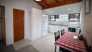 Een kleine keuken met witte kastjes, een houten plafond en een eethoek met een rood-wit geruit tafelkleed.