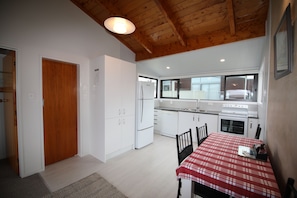 Een kleine keuken met witte kastjes, een houten plafond en een eethoek met een rood-wit geruit tafelkleed.