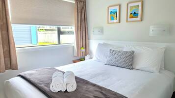Een hotelkamer met een bed, twee kussens, een dekbed, een raam met gordijnen en twee foto's in lijsten aan de muur.