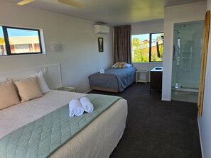 Une chambre d’hôtel avec deux lits, une petite table, un espace douche et une fenêtre donnant sur des immeubles et des arbres.