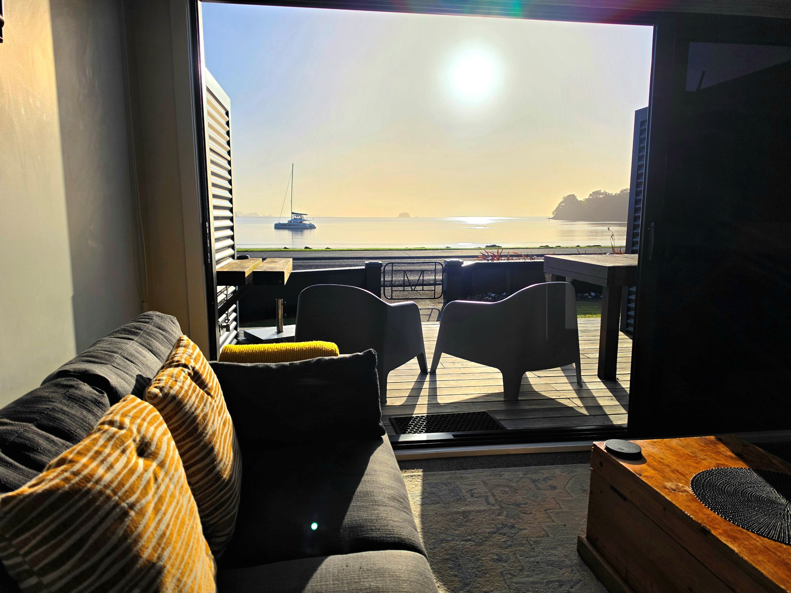 A living room with a view of the sea, a sofa, a table, and a television.