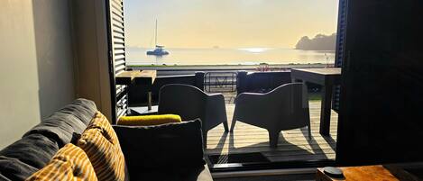 A living room with a view of the sea, a sofa, a table, and a television.