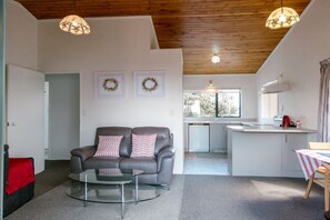 Uma sala de estar moderna com um sofá cinzento, uma mesa de centro de vidro e uma área de cozinha com uma pia e uma chaleira.